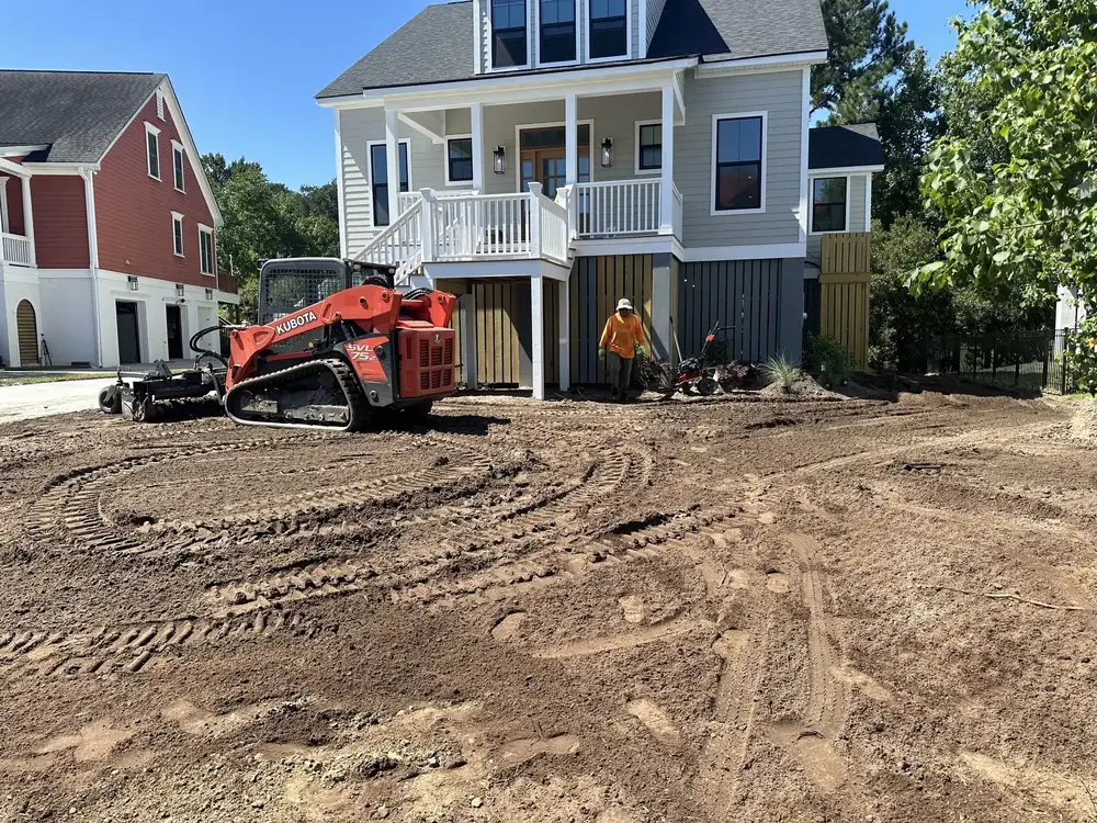 Track loader grading the lot beside a new raised house