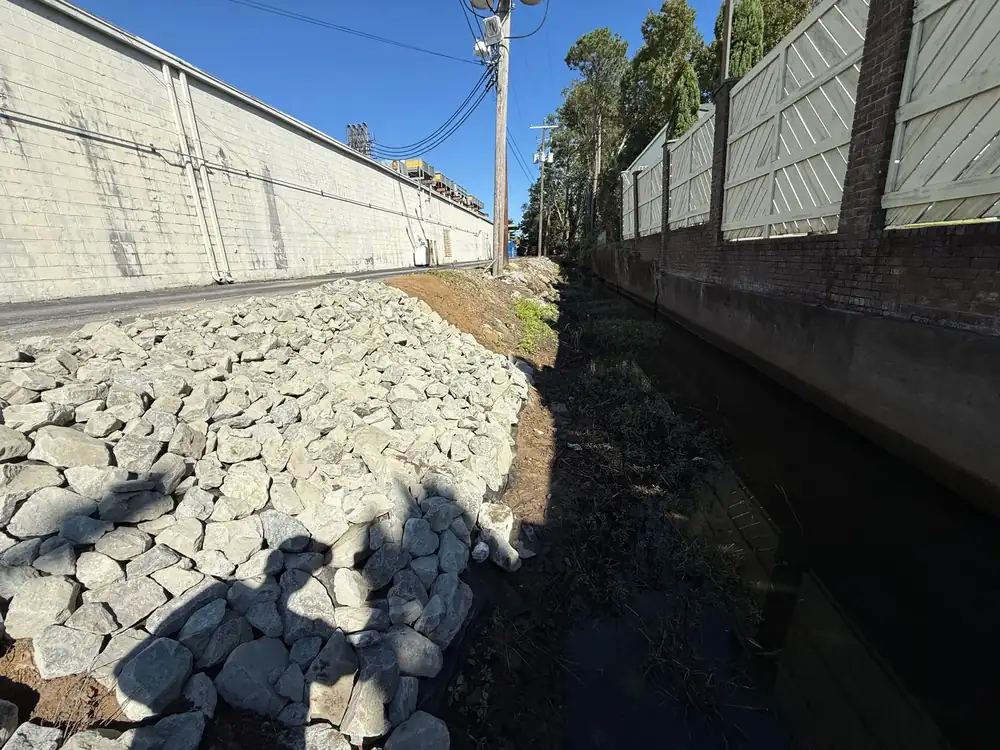 Rip-rap stone lining a drainage ditch beside a wall